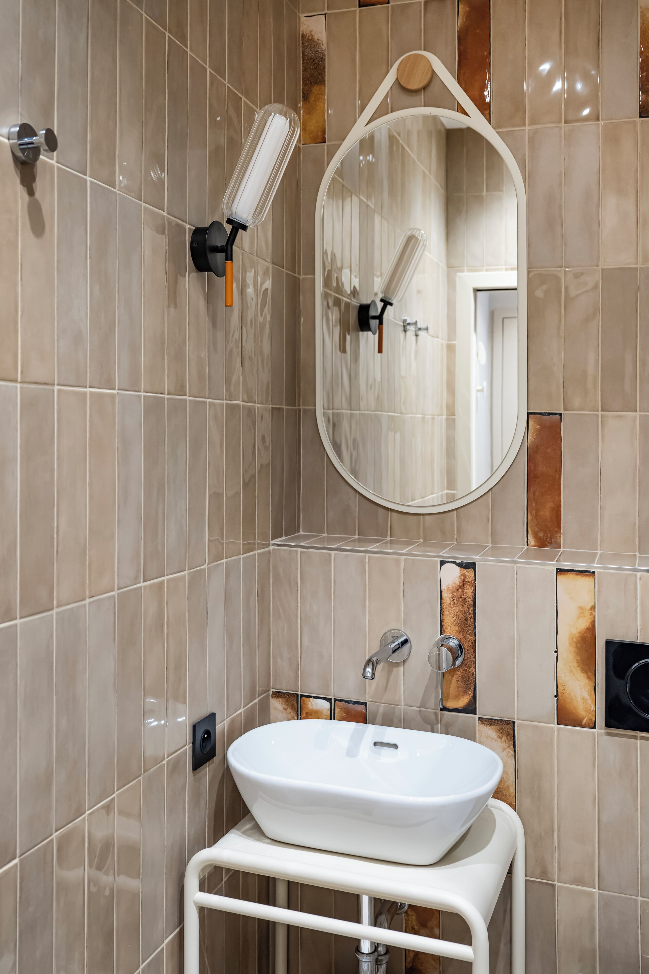 Un baño con un lavamanos blanco sobre un pedestal blanco, un espejo con marco de madera y paredes de baldosas color beige con algunos detalles marrones.