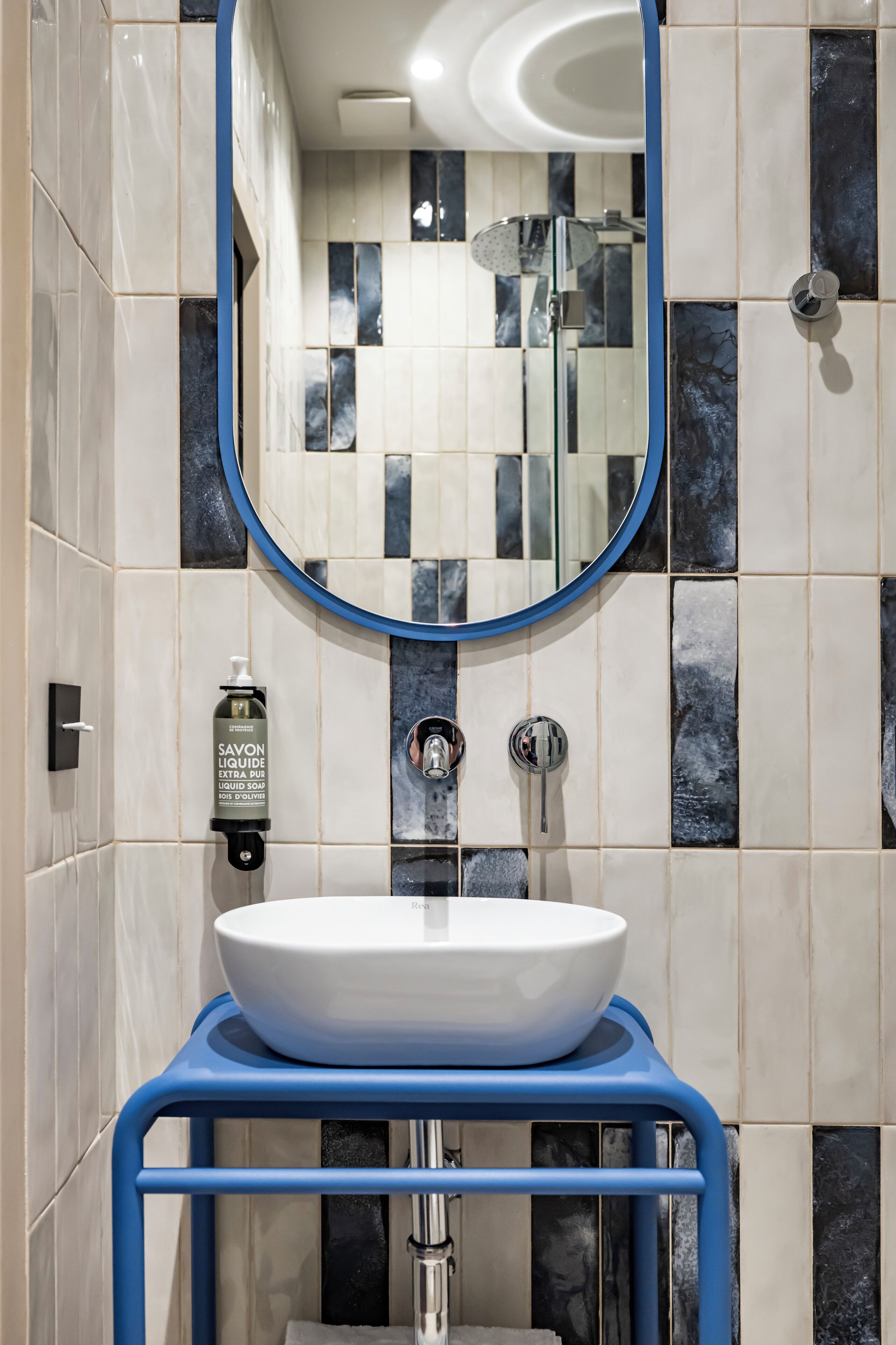 A bathroom with a white sink on a blue pedestal, a mirror above it, and a shower with a handheld showerhead.