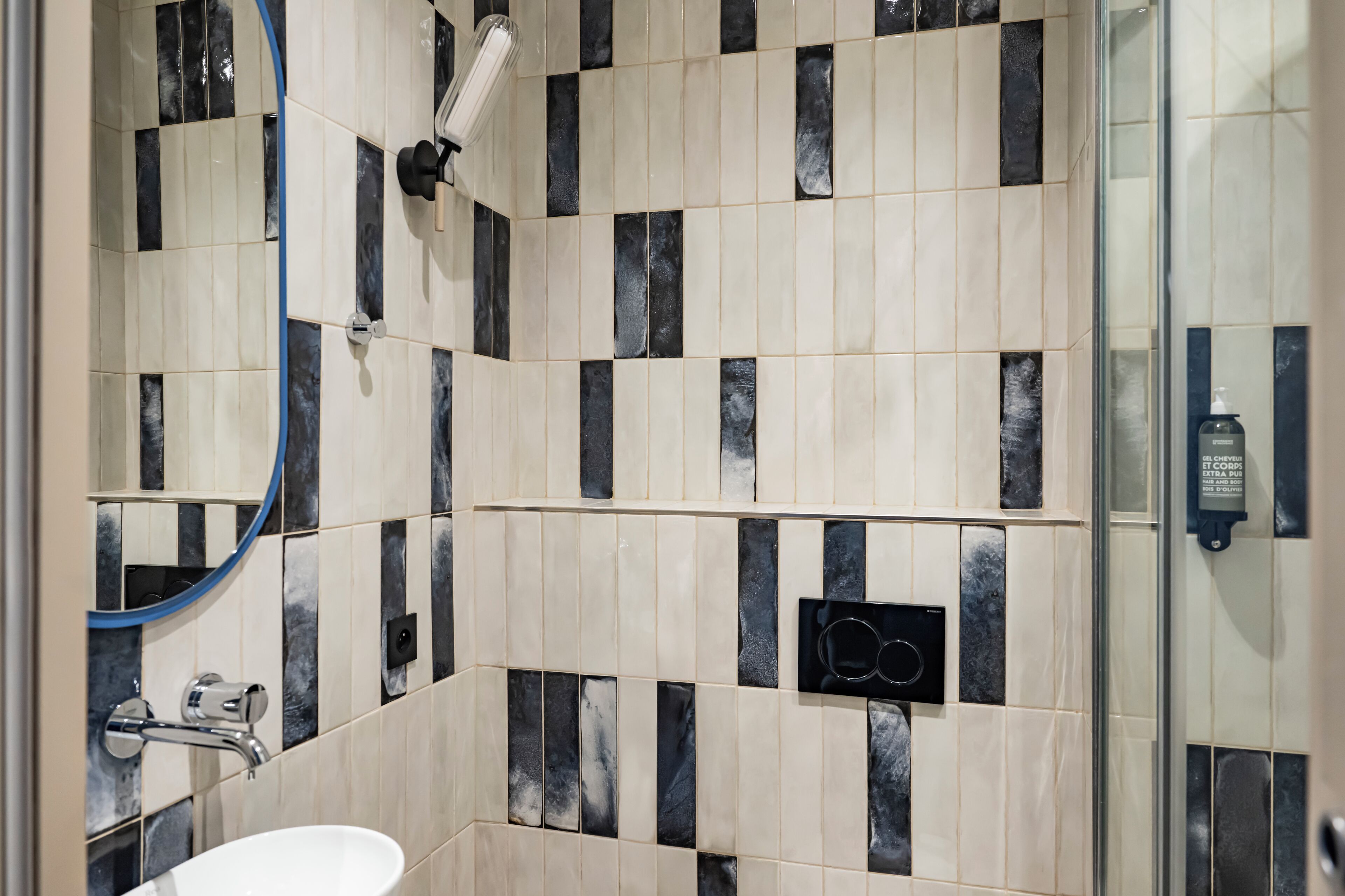A bathroom with a tiled wall, a mirror, a sink, and a shower area.