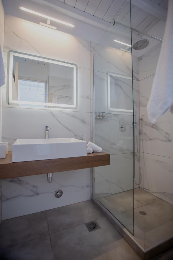 A modern bathroom with a white marble sink, a glass shower enclosure, and a wooden vanity.