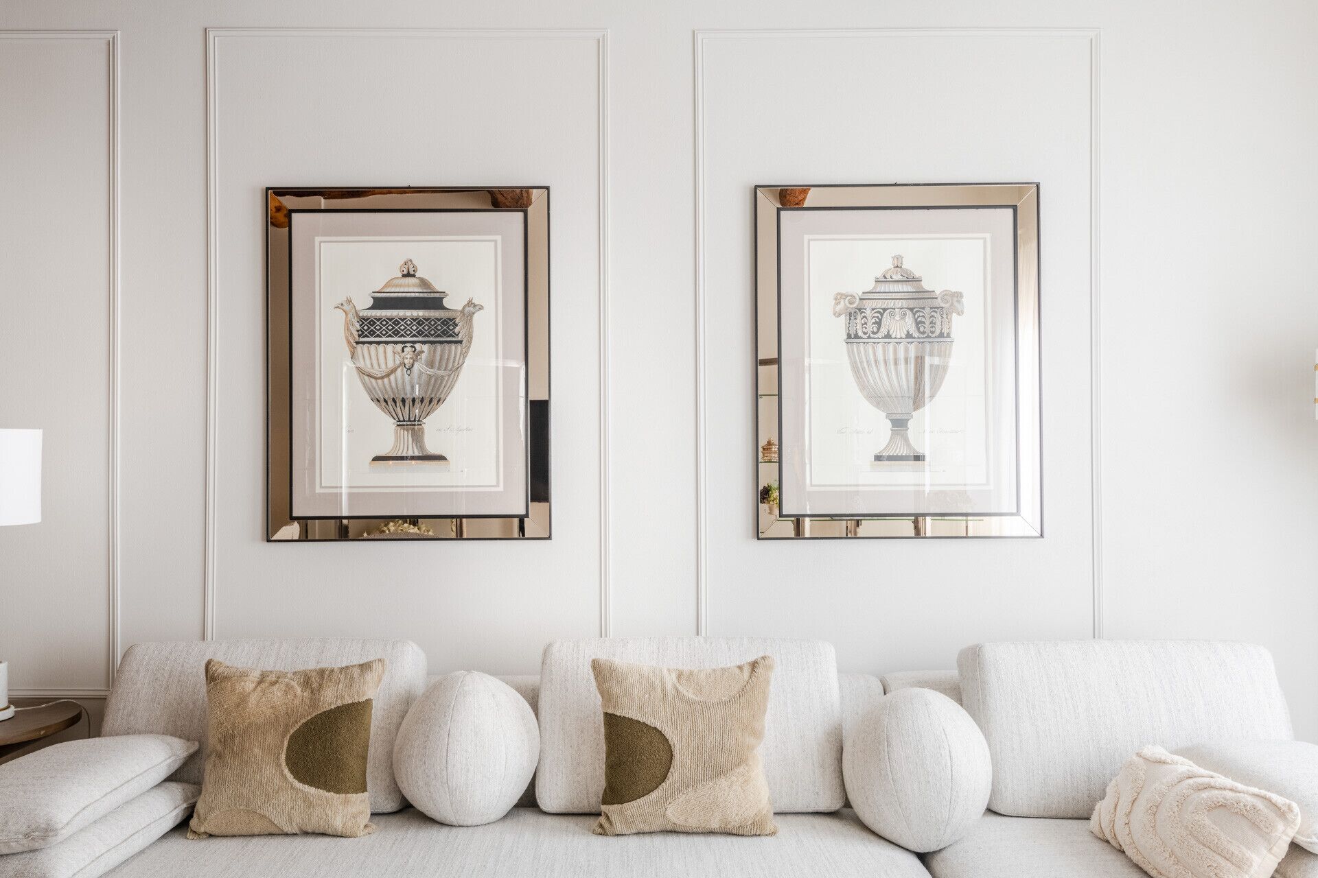 A room with a white sofa and two framed artworks depicting vases.