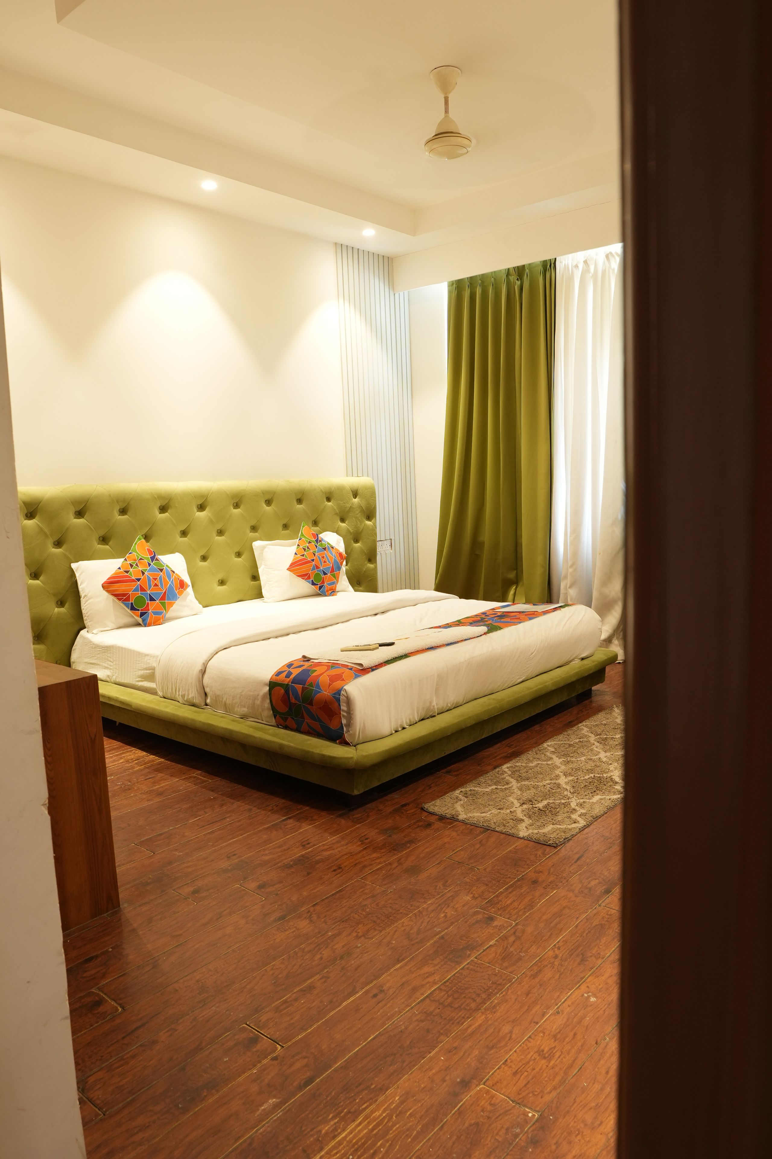 A bedroom with a green upholstered headboard, a wooden floor, and a bed with colorful pillows.