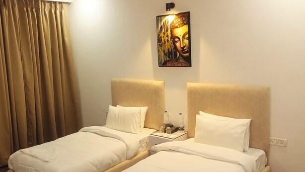 Quarto de hotel com duas camas, cortinas bege, pintura de Buda e mesa de cabeceira com garrafas de água.