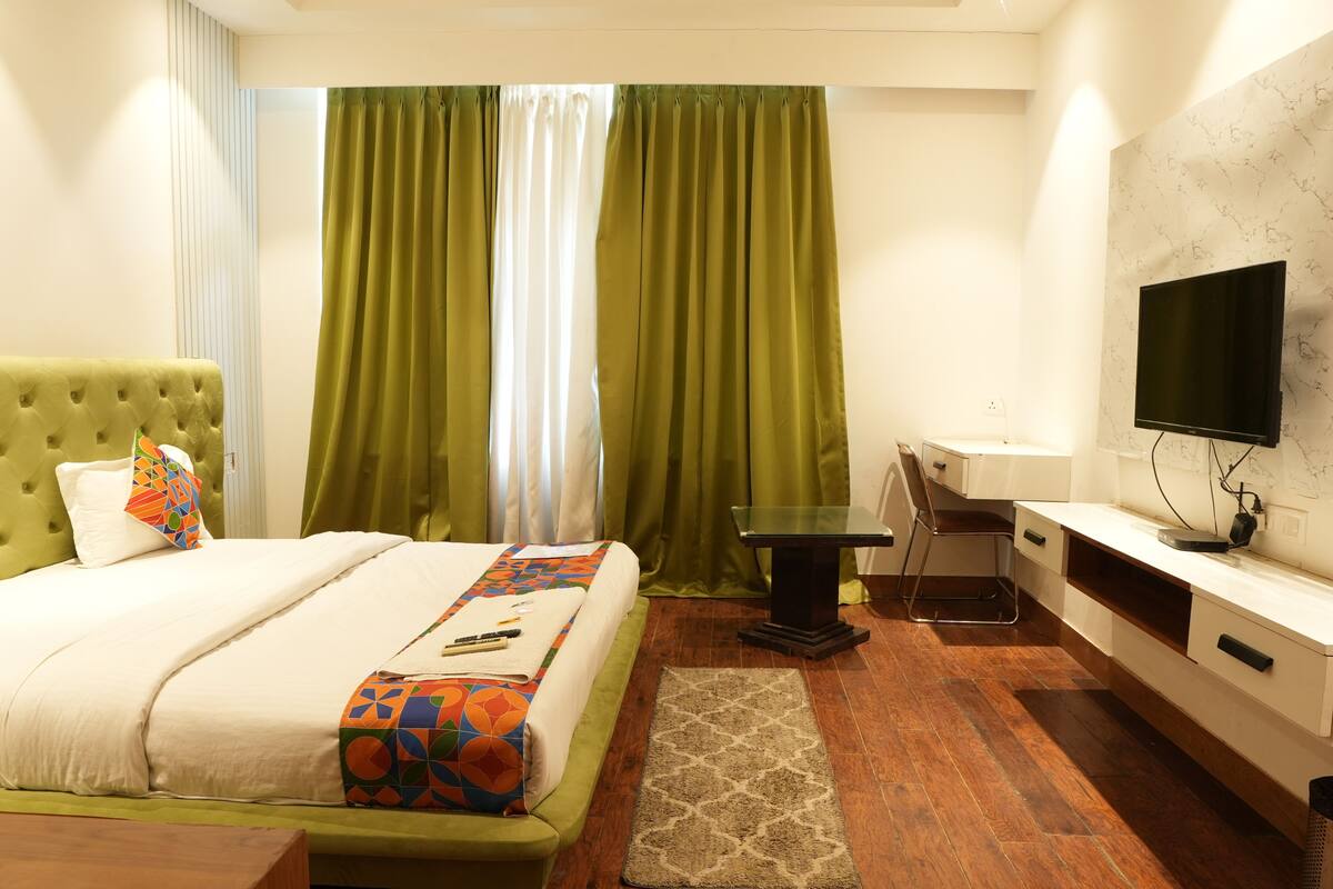 A hotel room with a bed, a desk, a chair, a TV, and a window with curtains.
