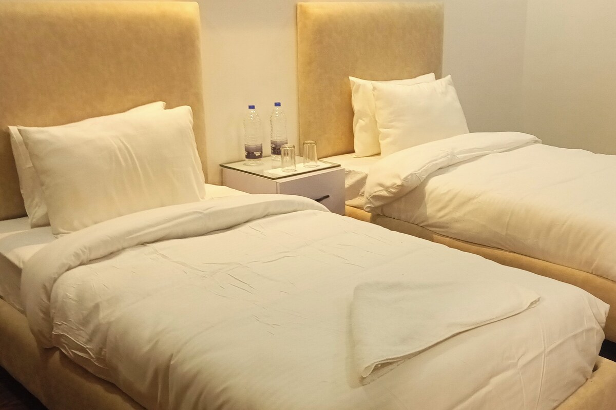 Two single beds with headboards, a nightstand with a lamp, and two water bottles on the nightstand.