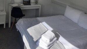 Une chambre d’hôtel avec un lit, un bureau équipé d’un ordinateur, une chaise et un tableau représentant des voiliers accroché au mur.