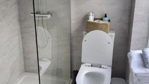Une salle de bain moderne avec une douche à parois de verre, des toilettes et un petit panier en osier contenant des articles de toilette.