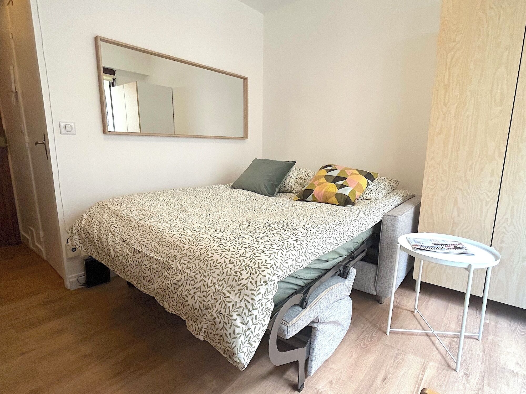 Une chambre à coucher avec un lit, une petite table, un miroir et une armoire.