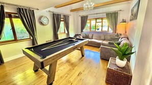 A pool table in a room with a sofa, a chandelier, and a clock on the wall.