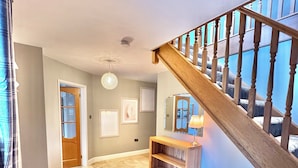 A spacious hallway with a wooden staircase, a chandelier, and a console table.