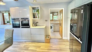 A modern kitchen with built-in appliances, a dining area with a chair, and a laundry room visible through an open doorway.