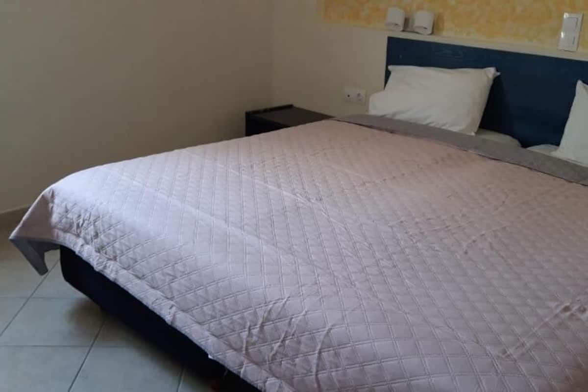 Cama com cobre acolchoado, mesa de cabeceira e luminária fixada na parede.