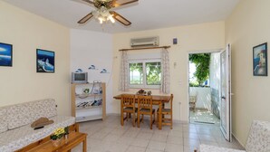 A living room with a sofa, a wooden dining table with chairs, a ceiling fan, and a television. - Crete Essence Villas-Makrygialos (Ierapetra)