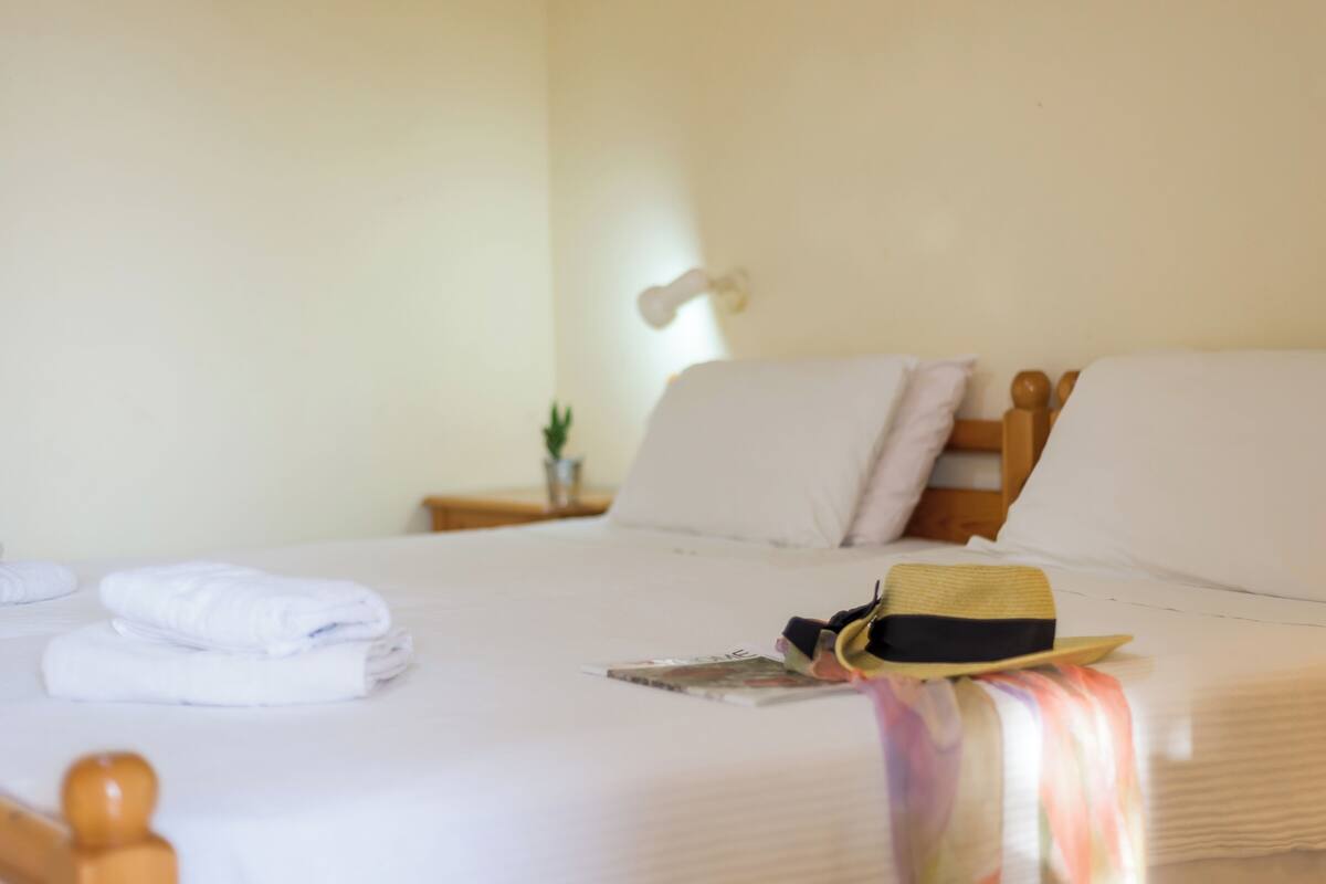 Uma cama bem arrumada com lençóis brancos, uma toalha dobrada e um chapéu sobre os travesseiros.