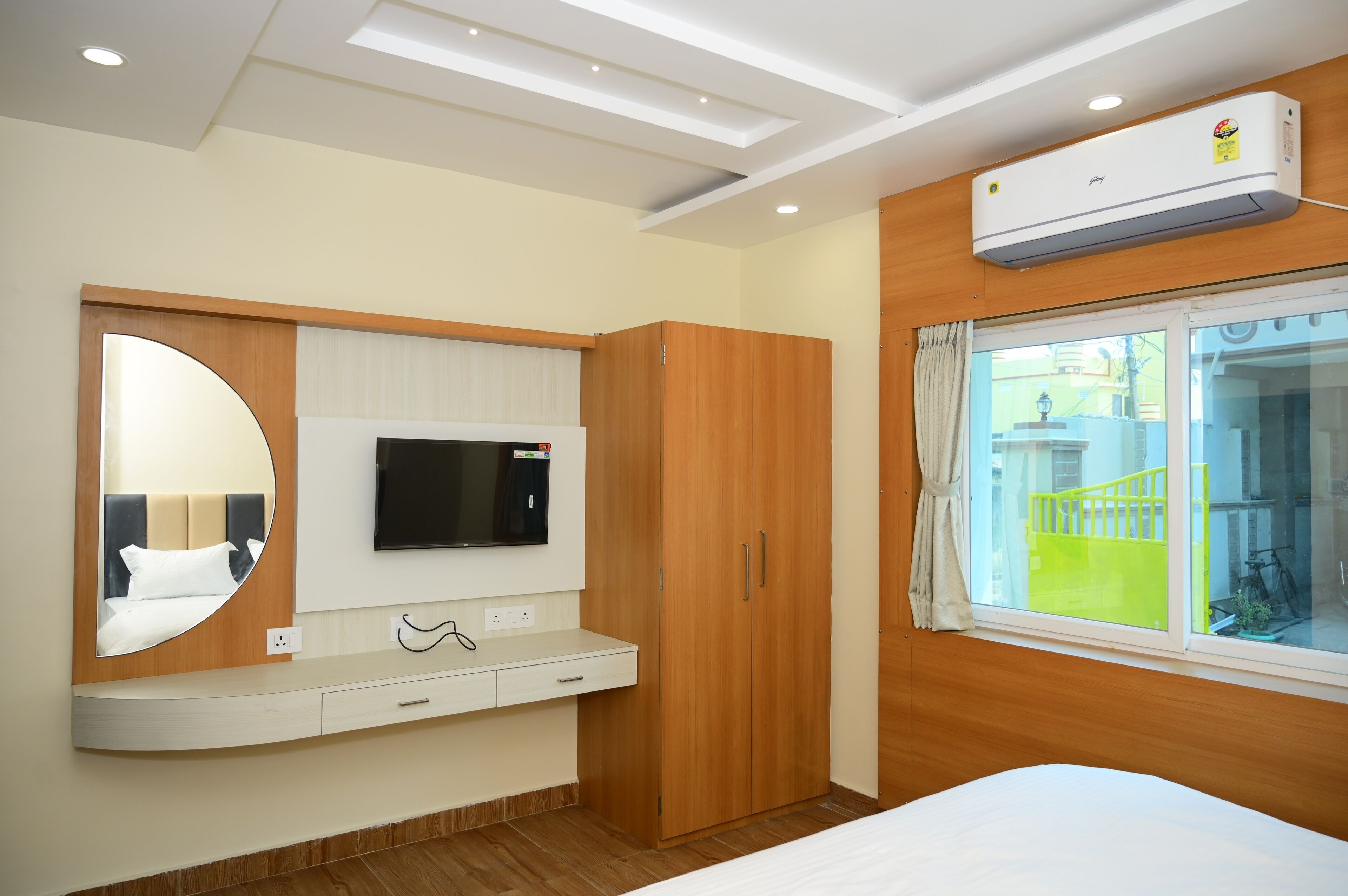 Una camera d'albergo con un letto, una TV fissata a un pannello di legno, un armadio, uno specchio e una finestra con vista su una zona verde.