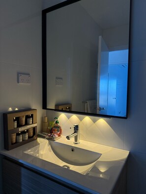 A bathroom with a white sink, a mirror, and a shelf with toiletries.