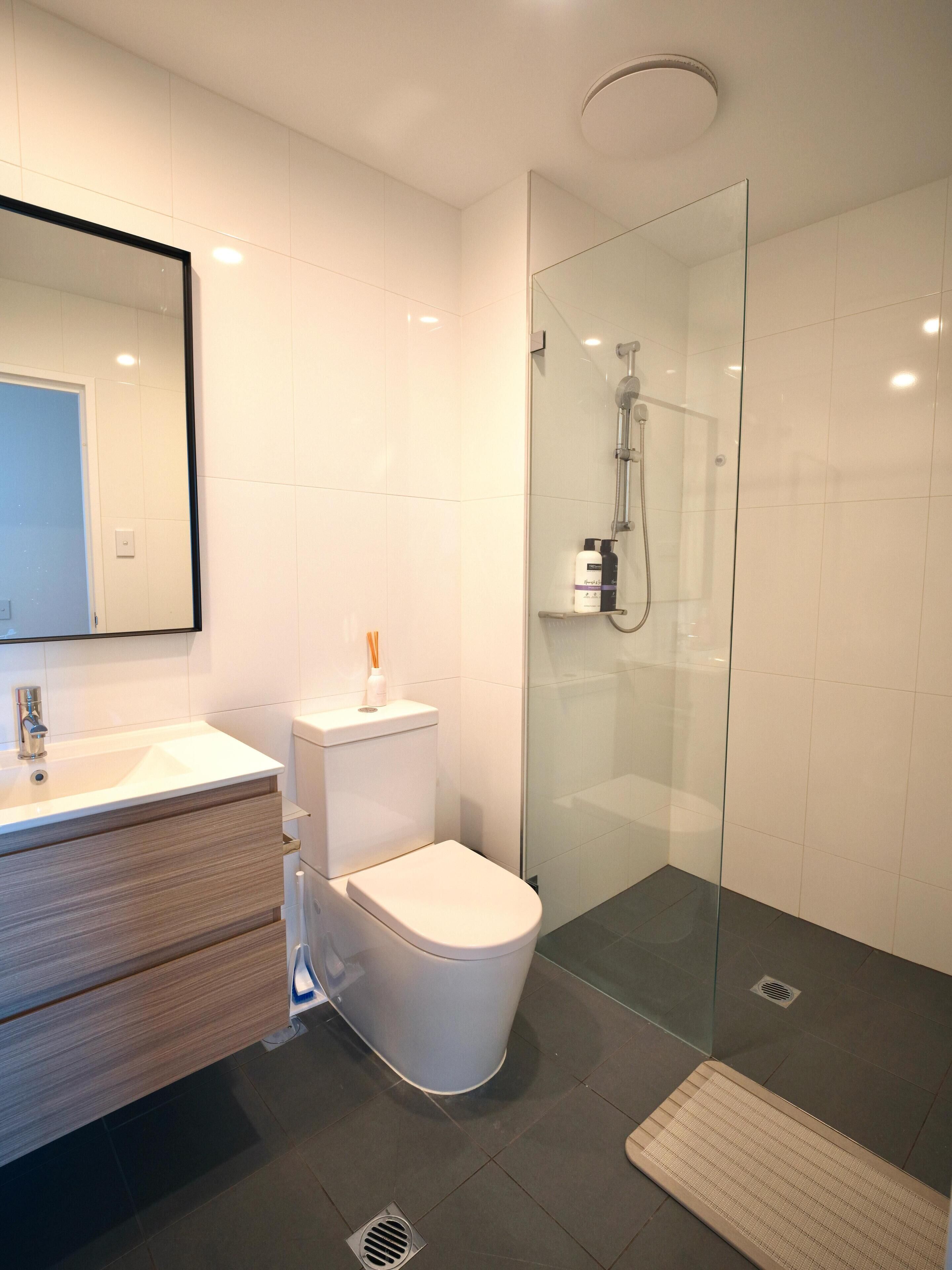Een moderne badkamer met een douchecabine van glas, een wit toilet en een wastafel met spiegel.