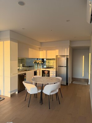 A modern kitchen with white cabinetry, a stainless steel refrigerator, and a round dining table with white chairs.