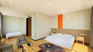 A modern hotel room with a large bed, a smaller bed, a desk, and a sofa.