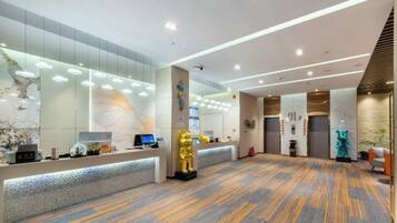 A modern hotel lobby with a reception desk, a large golden statue, and a patterned carpet.
