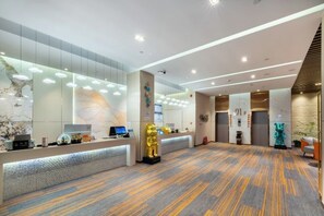 A modern hotel lobby with a reception desk, a large golden statue, and a patterned carpet.