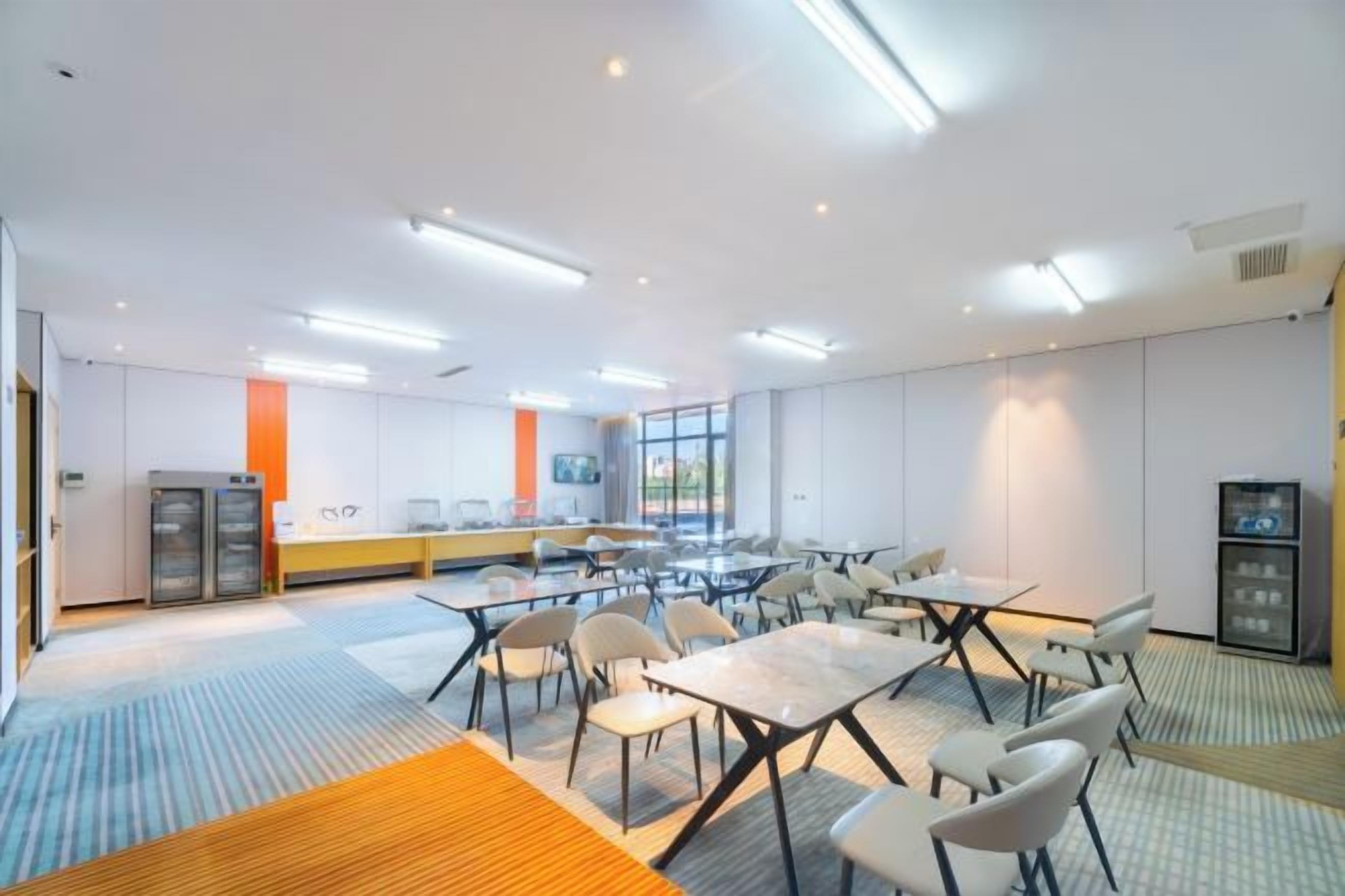 Een moderne vergaderruimte met tafels, stoelen, een groot raam en een kitchenette.