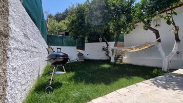 Un patio trasero con una parrilla, una hamaca y un pequeño árbol.