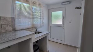 Et lille køkken med vask, et vindue med skodder, et køleskab og en dør med frostet glas.