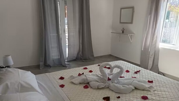 A hotel room with a bed, a bedside table, a mirror, and a window with curtains.