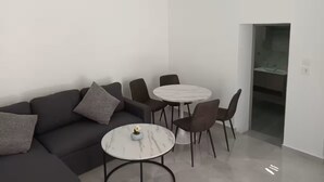 A modern living room with a sectional sofa, a round dining table with chairs, and a built-in kitchen area.