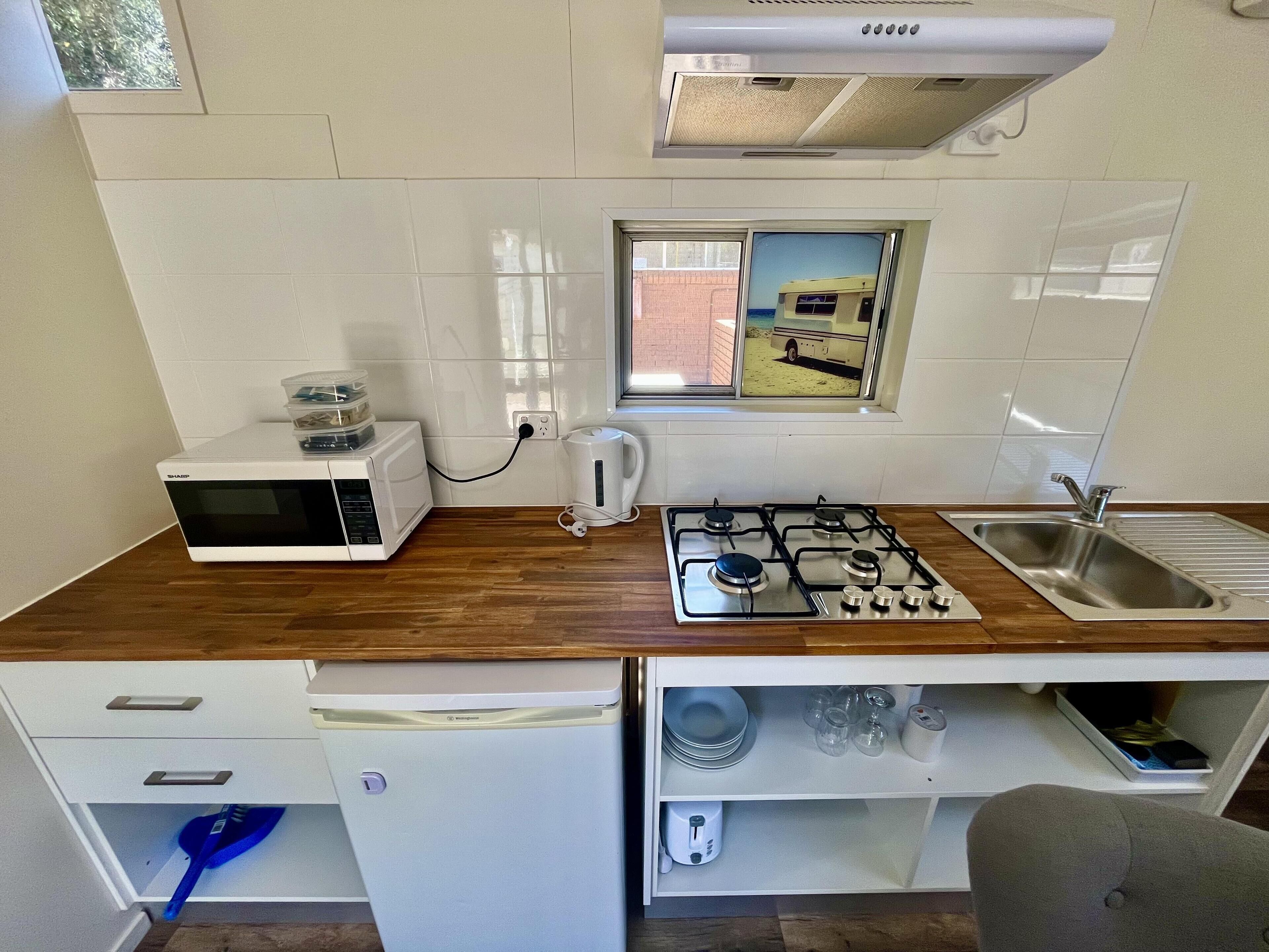 A compact kitchen with a microwave, gas stove, sink, and a small refrigerator.