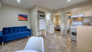 A compact room with a blue sofa, a white chair, a kitchenette with a stove, and a bed in the background. - Westview Caravan Park - Dubbo (Dubbo)
