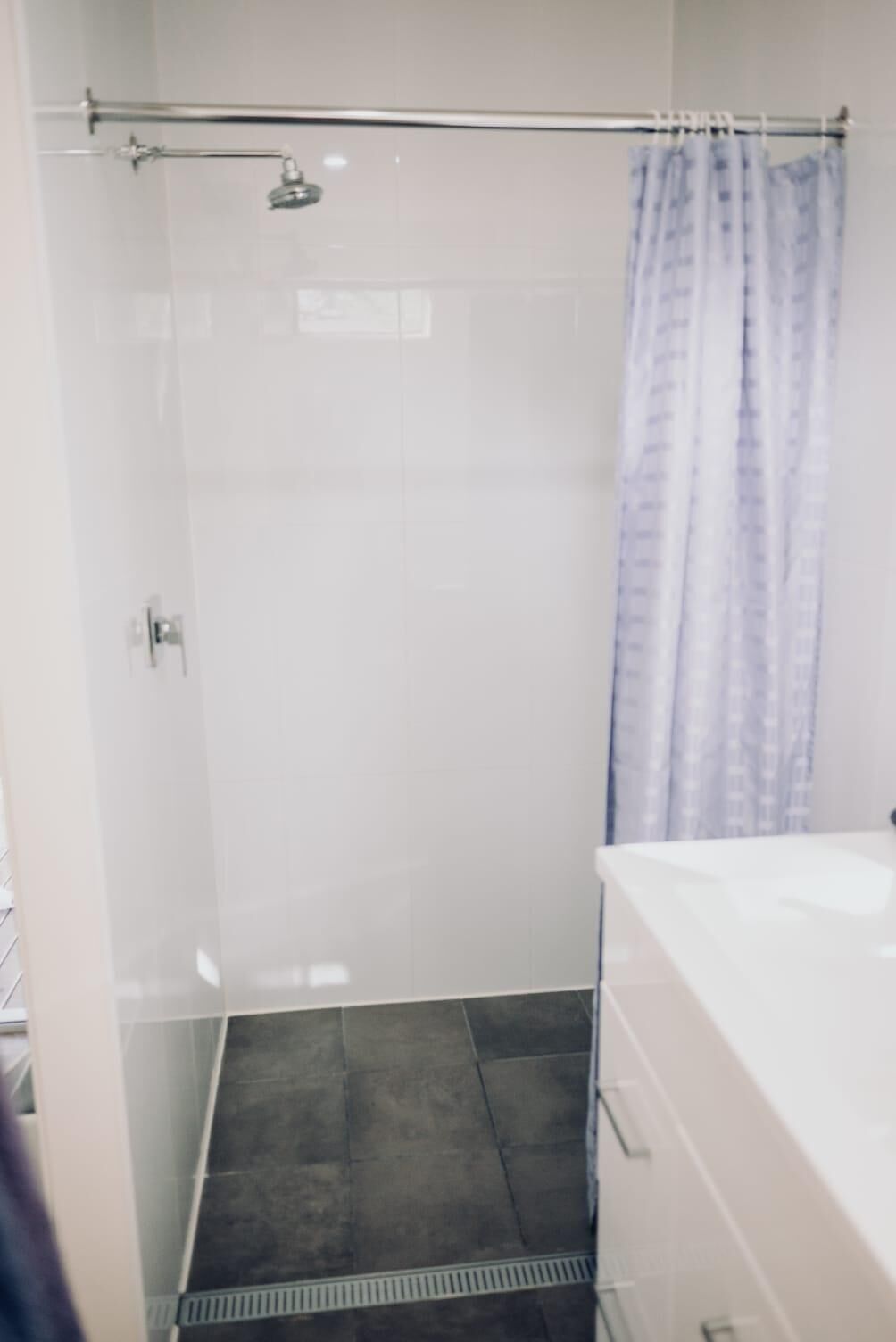 A bathroom with a shower, a glass door, a white sink, and a patterned shower curtain.