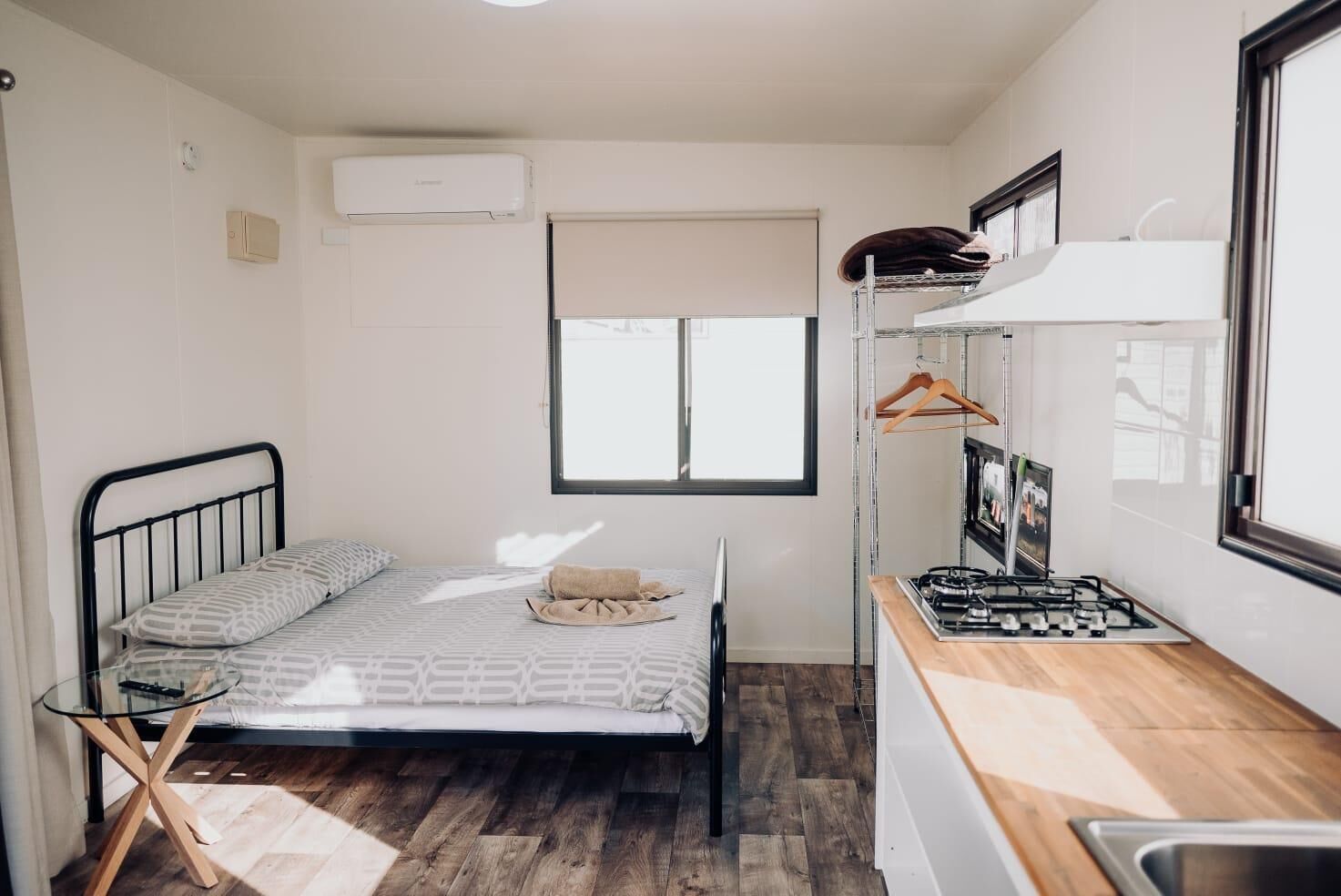Een kleine kamer met een bed, een tafeltje, een kitchenette en een raam.