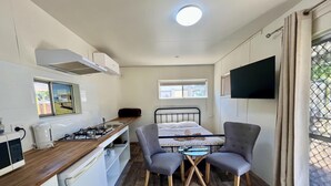 A compact kitchenette with a stove, sink, and small refrigerator. There is a bed with a TV mounted above it, and a window providing natural light. - Westview Caravan Park - Dubbo (Dubbo)
