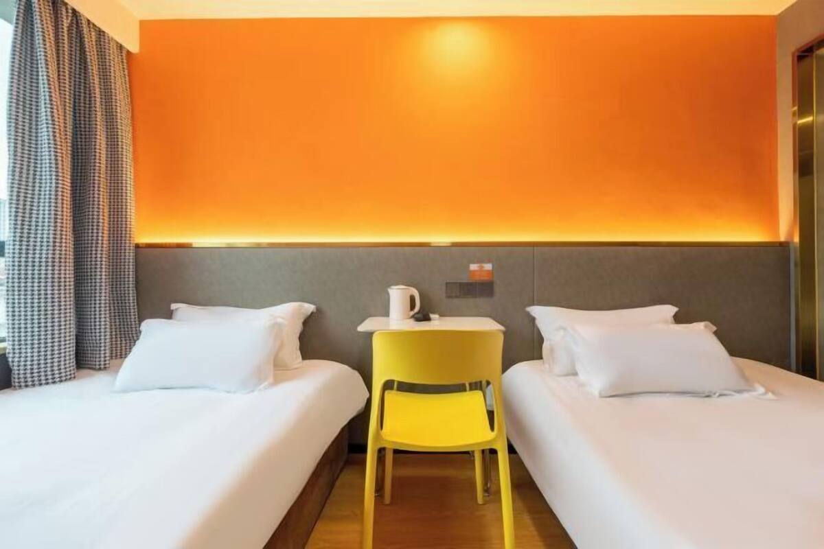 Ett hotellrum med två sängar, ett litet bord med en kopp på och en gul stol.