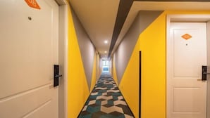 A hotel corridor with a geometric patterned carpet, yellow and white walls, and doors marked with room numbers.