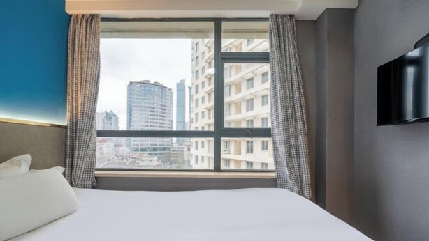 A hotel room with a large window, a bed, and a flat-screen TV mounted on the wall.