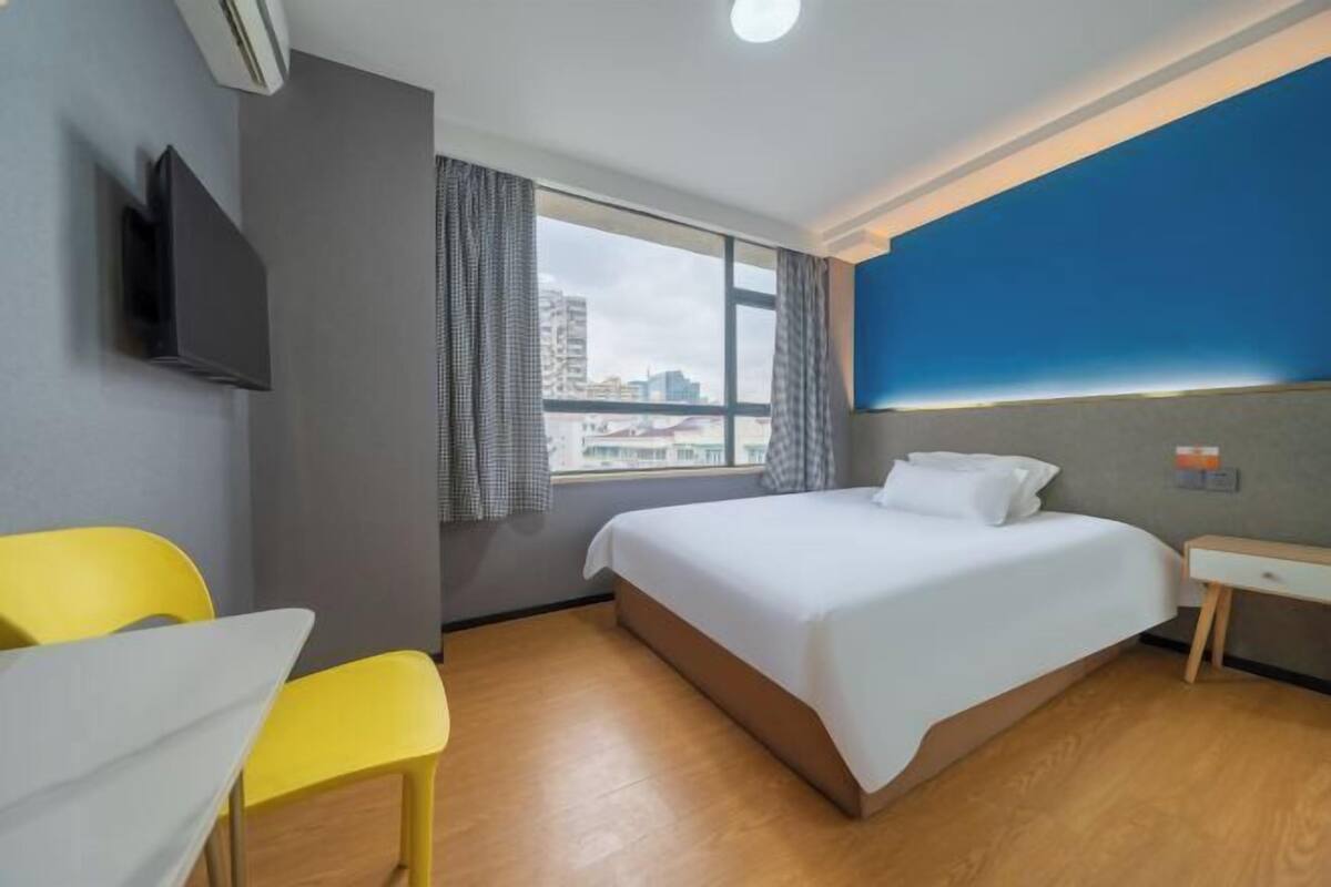 Ett hotellrum med en säng, ett skrivbord, en stol, en tv och ett fönster med gardiner.