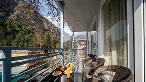 A balcony with wicker chairs, a table with a basket of fruit and a glass of orange juice, and a mountain view. - Abhilashi Inn Kasol (Kasol)