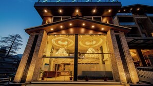 A modern building with a prominent entrance, large glass windows, and a balcony with railings. - Abhilashi Inn Kasol (Kasol)