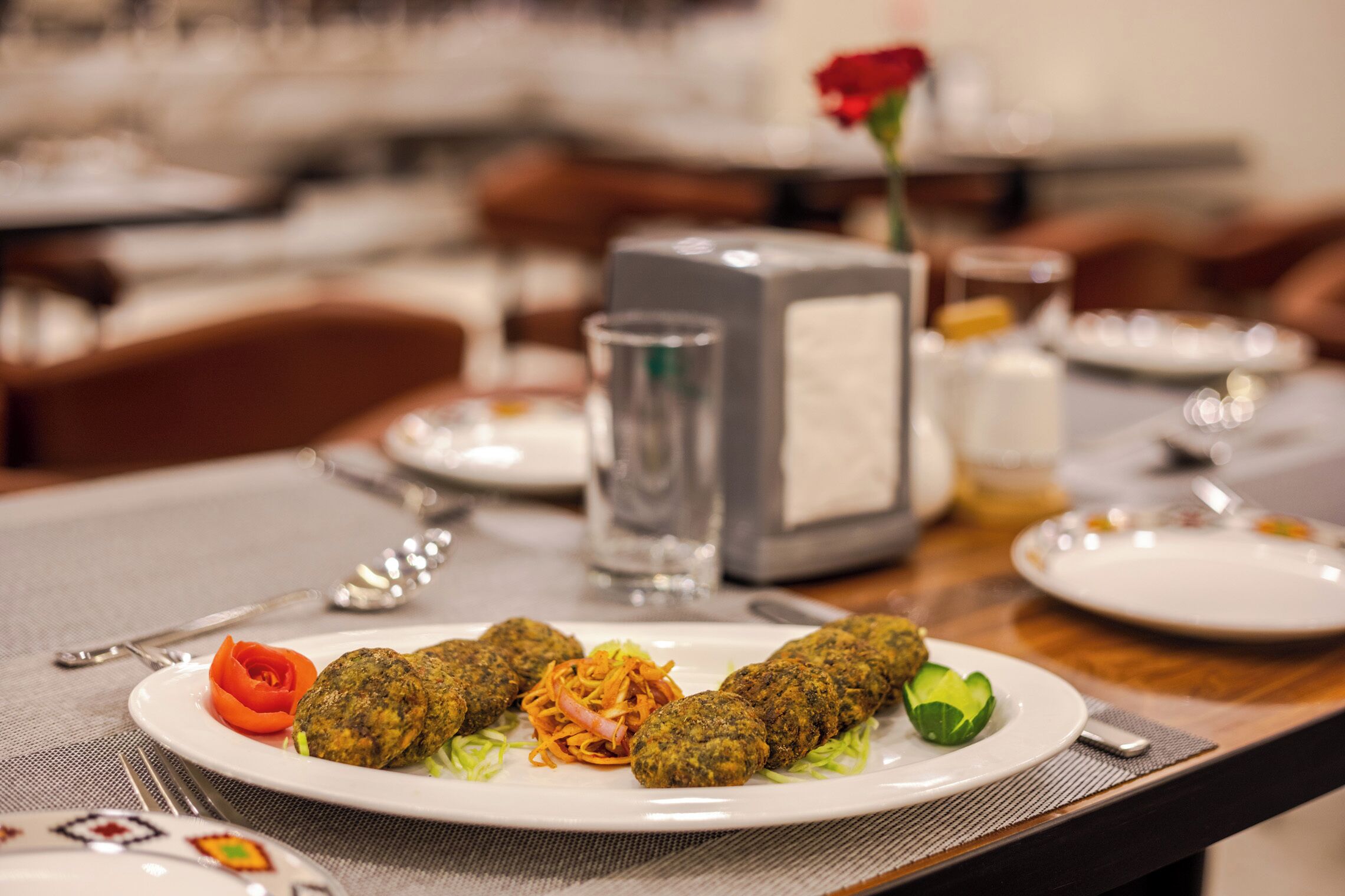 A dining table with a plate of falafel, a rose, and a glass of water.