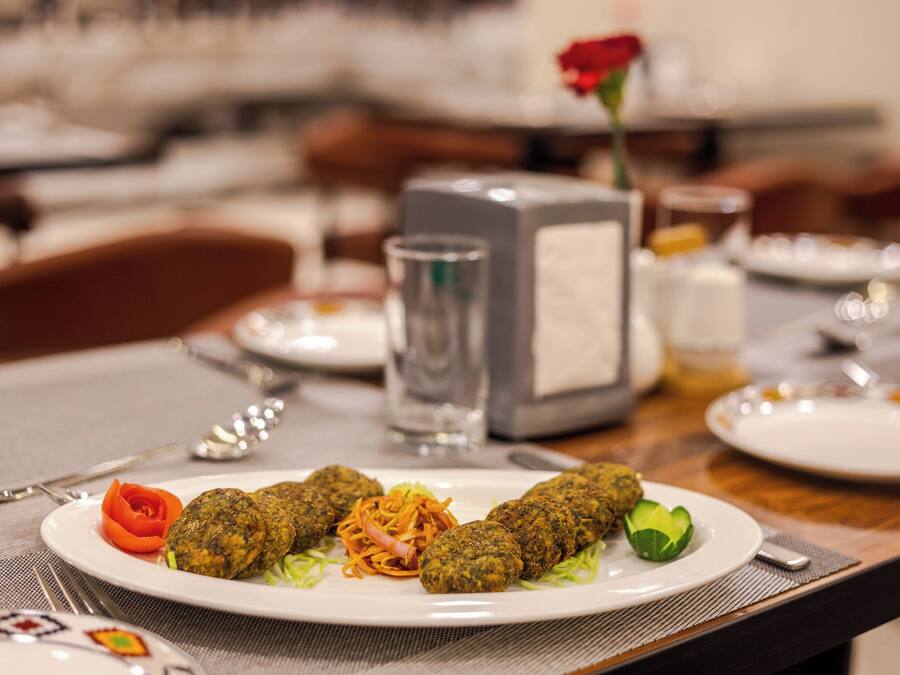 A dining table with a plate of falafel, a rose, and a glass of water.