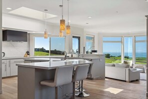 A modern kitchen with a large island, bar stools, and a view of the ocean.