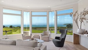 A modern living room with large windows, a telescope, and a view of the ocean.