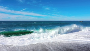 A beach with waves crashing onto the shore, clear blue sky, and calm sea.