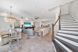 Una sala de estar amplia con un televisor grande, un comedor con mesa y sillas de madera, y una escalera de diseño moderno.