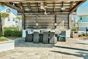 Eine Terrassengruppe mit überdachtem Grillbereich, Korbmöbeln und Deckenventilator.