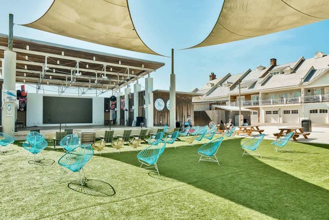 A hotel with a covered outdoor seating area, a stage, and a poolside lounge with chairs.