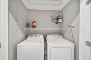 A laundry room with two Whirlpool washers and dryers, a fire extinguisher, and a metal exhaust fan on the wall.